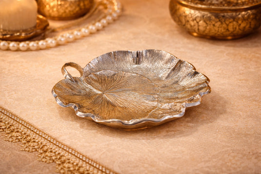 Decorative leaf-shaped silver dish on a textured surface with gold accents